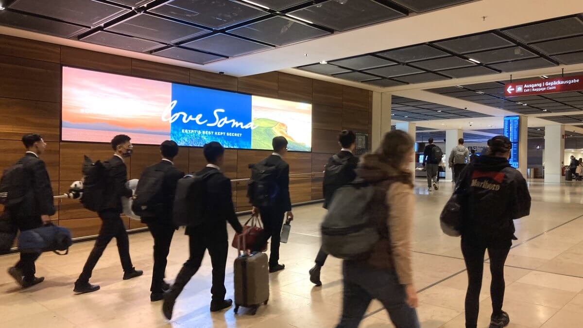 Am Ankommergang von Terminal 1 des BER Flughafen in Berlin präsentiert sich Somabay auf einem Coloramen. Ihr Motiv zeigt die eigenartige Landschaft Ägyptens. Es laufen Passagiere an der Werbung vorbei zur Gepäckausgabe.