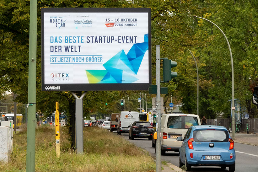 Ein digitaler City Light Board auf einer Hauptstraße mit viel Verkehr in Berlin. Es zeigt eine Werbung über ein Start-up Event.