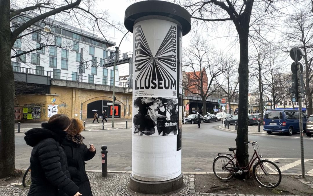 Am Savignyplatz in Berlin steht eine Litfaßsäule mit der Plakatwerbung von der Tanzgruppe Cie.Toula. Mit ihrer Kampagne werben sie für ihr neues Stück „Staubkinder“. Man sieht den Bahnhof, Autos und Fahrräder, sowie Fußgänger vorbeilaufen.